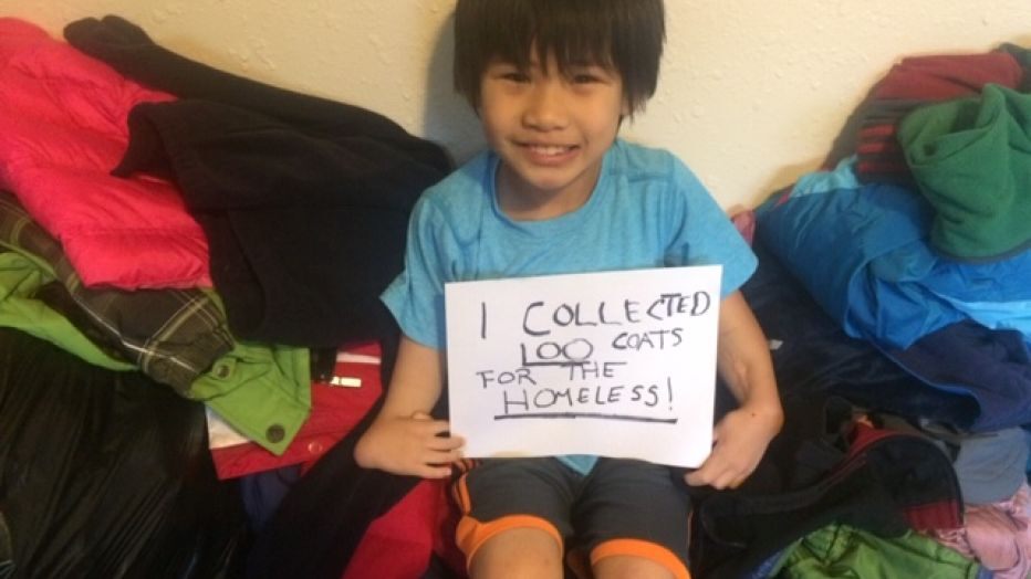 Young boy holding a sign that reads states he collected 100 coats for the homeless